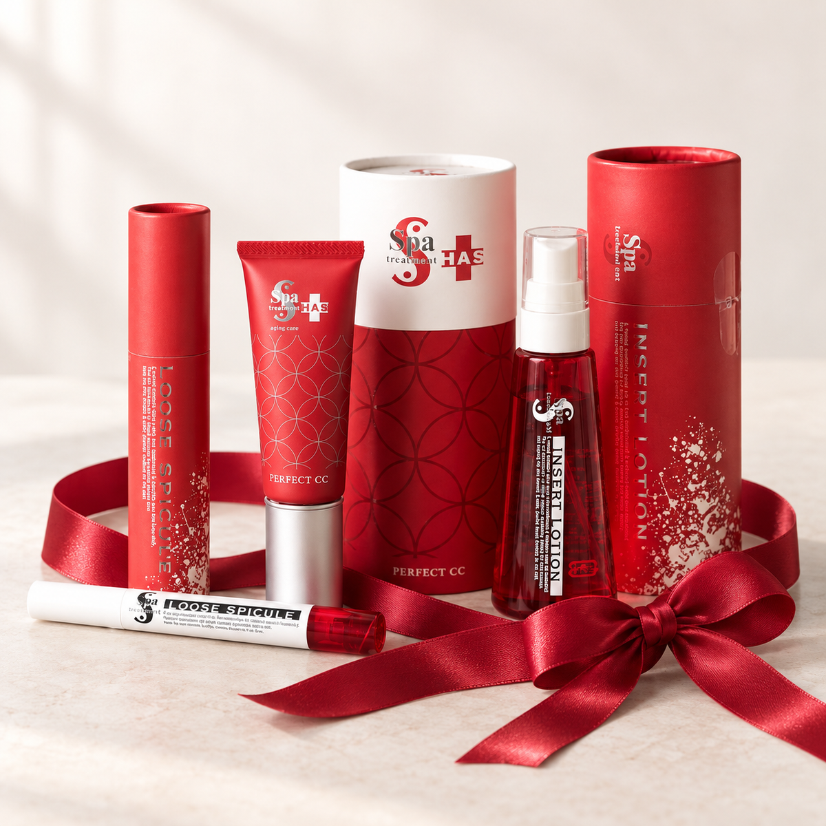 Japanese Cosmetics – prezentowy zestaw kosmetyków Spa Treatment HAS z produktami Perfect CC, Insert Lotion i Loose Spicule, ozdobiony czerwonym satynowym kokardą na jasnym tle.